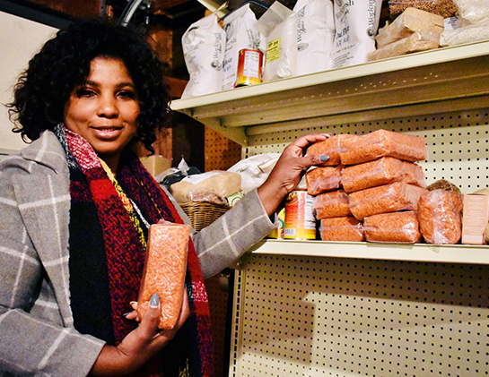 Nathalie holds up a package of red lentils next to shelves holding more groceries