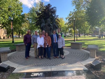 A group of board members gathers around the statue of the Hutchinson Brothers