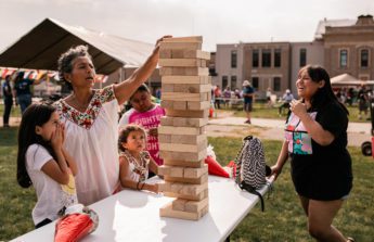 A group of kids and an adult build a tower out of giant blocks on a table outdoors.