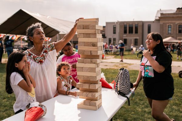 A group of kids and an adult build a tower out of giant blocks on a table outdoors.