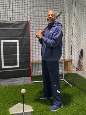 Darryl holds a baseball bat and stands inside a batting cage