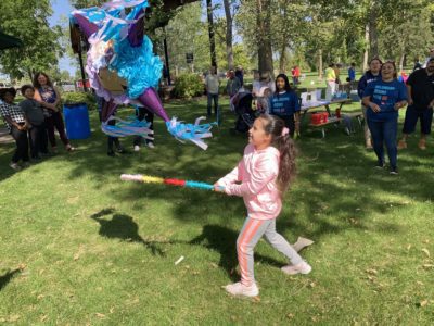 A girl swings a stick at a pinata at an outdoor celebration