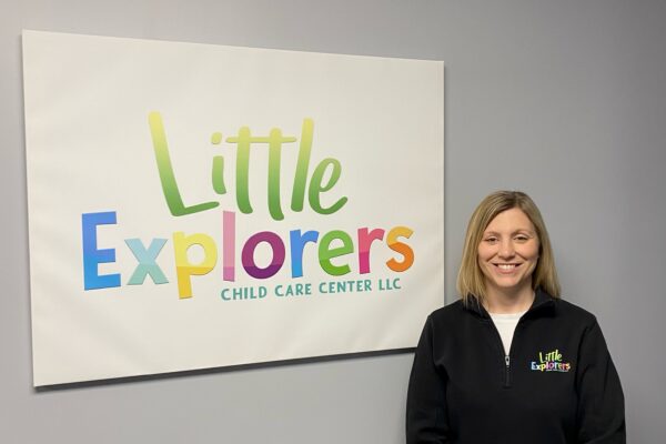 Jamie stands next to an indoor sign for Little Explorers Child Care Center