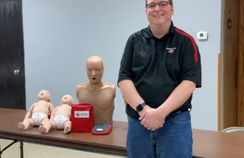 Ray stands next to a table with an AED and several first aid mannequins.