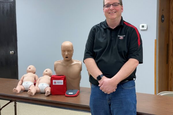Ray stands next to a table with an AED and several first aid mannequins.
