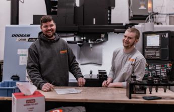 Mark and Tobias stand behind a table inside their shop, Metal Trade Solutions.