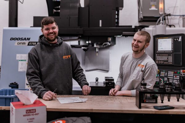 Mark and Tobias stand behind a table inside their shop, Metal Trade Solutions.