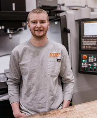 Tobias stands in front of the DNM 6700 vertical machining center on the shop floor.