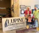 Tracee and Jeff hold golden shovels and pose with their two young daughters next to a sign for their new business, Lupine Construction