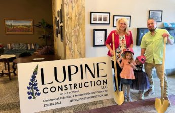 Tracee and Jeff hold golden shovels and pose with their two young daughters next to a sign for their new business, Lupine Construction