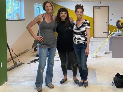 Katie Luoto, Kayla Swenson and Emily Allen stand with their arms around each other in a space that's being remodeled.