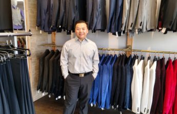 Sean stands in front of two racks of suit jackets in a variety of colors.