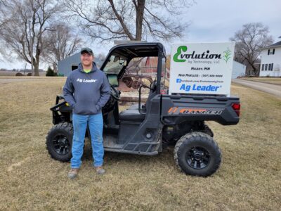 Nick stands outdoors next to a side-by-side vehicle with his business sign mounted in the back.