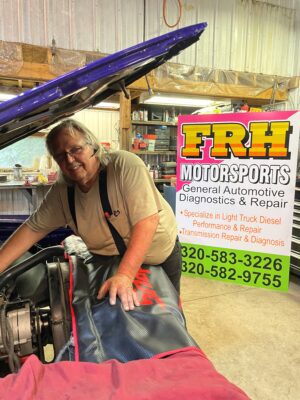 Fred leans over an engine under and open hood in his shop