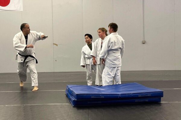 Three students watch Javier demonstrate a move inside the martial arts studio