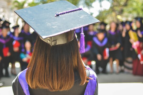 A graduate in cap and gown pictured from behind facing a group of fellow graduates.