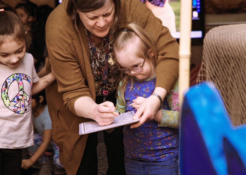 An adult helps a little learner fill in their scavenger hunt worksheet at the Discovery Room.
