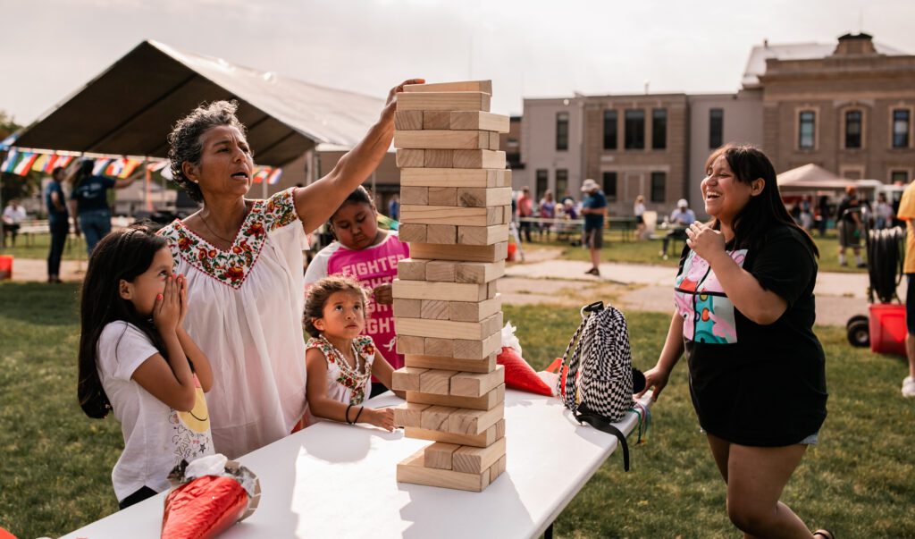 Woman and children laughing while stacking blocks in a yard game