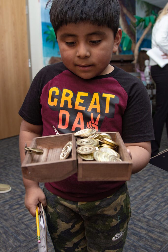 A child holds open a small treasure chest with large golden coins inside.