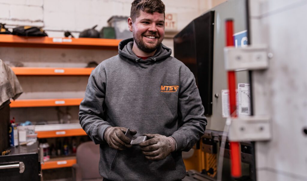 Smiling man working at Metal Trade Solutions holding a piece of metal.