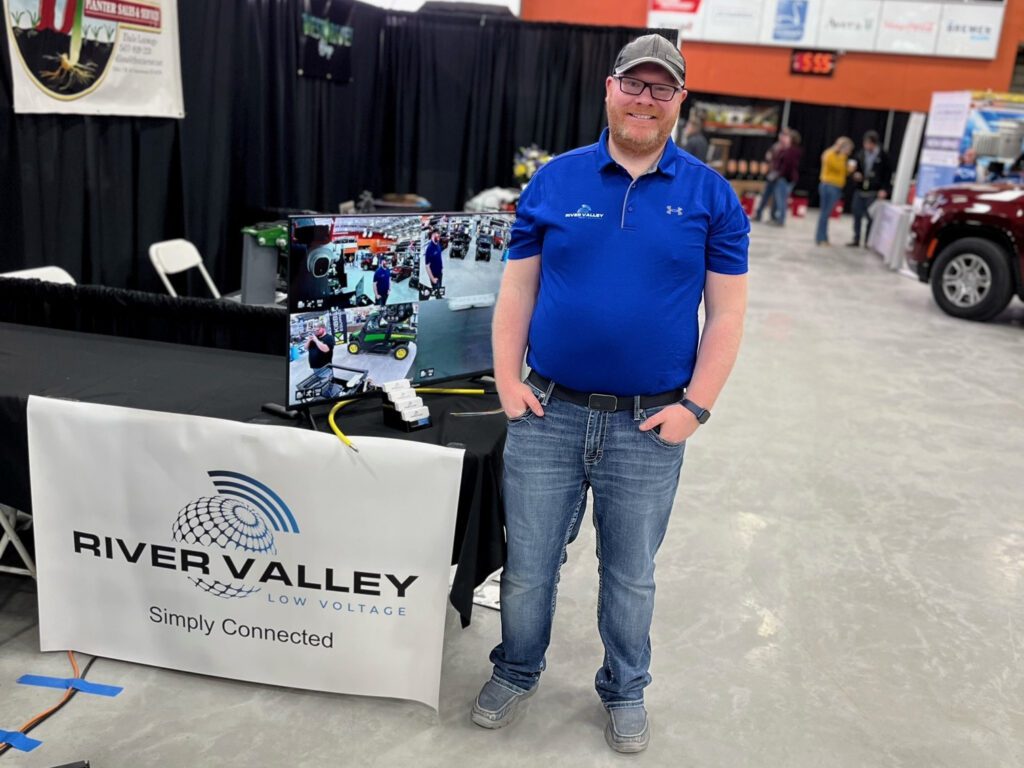 Harley stands next to an industry conference booth display for River Valley Low Voltage.