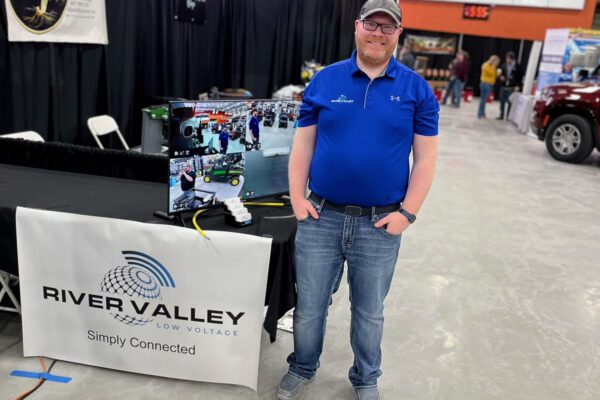 Harley stands next to an industry conference booth display for River Valley Low Voltage.
