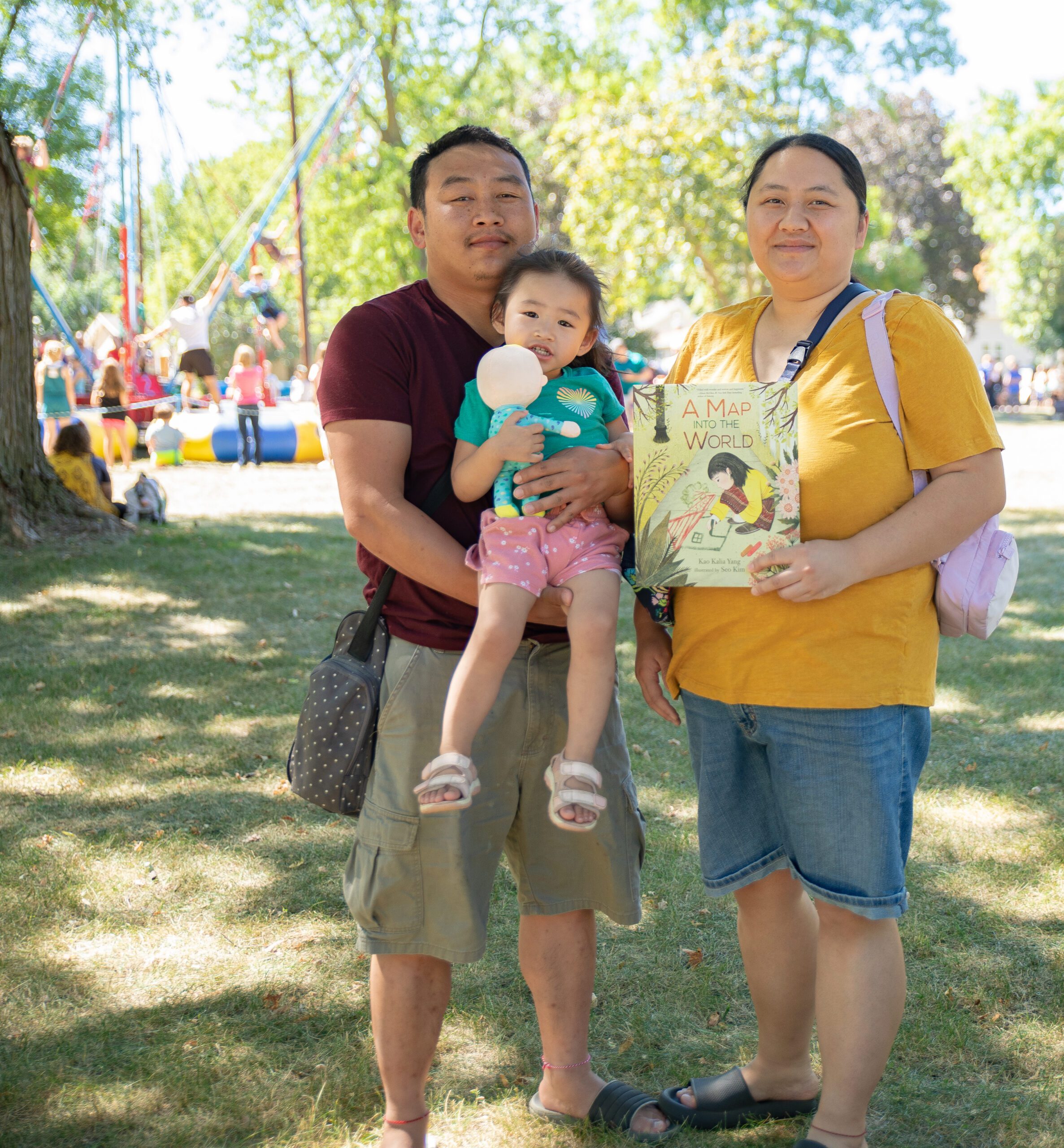 a couple holding their young child and a children's book at an outdoor event