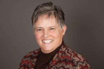 Theresa poses for a formal head shot wearing a brown mock turtleneck and patterned woven jacket.