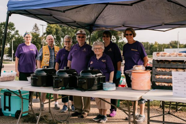 A group of volunteers wearing purple Lions Club T-shirts serves food at a community block party.