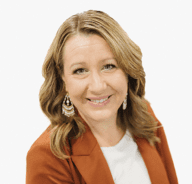 A woman with wavy, shoulder-length blonde hair smiles at the camera. She wears a rust-colored blazer, white top, and large, dangling earrings, set against a plain white background.