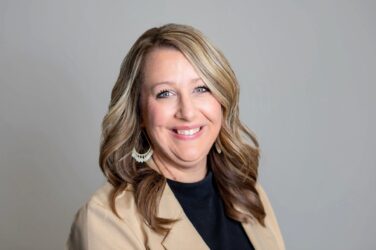 Briana poses for a formal head shot in front of a gray background.