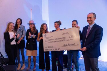 A group of people gather around a giant check to celebrate.