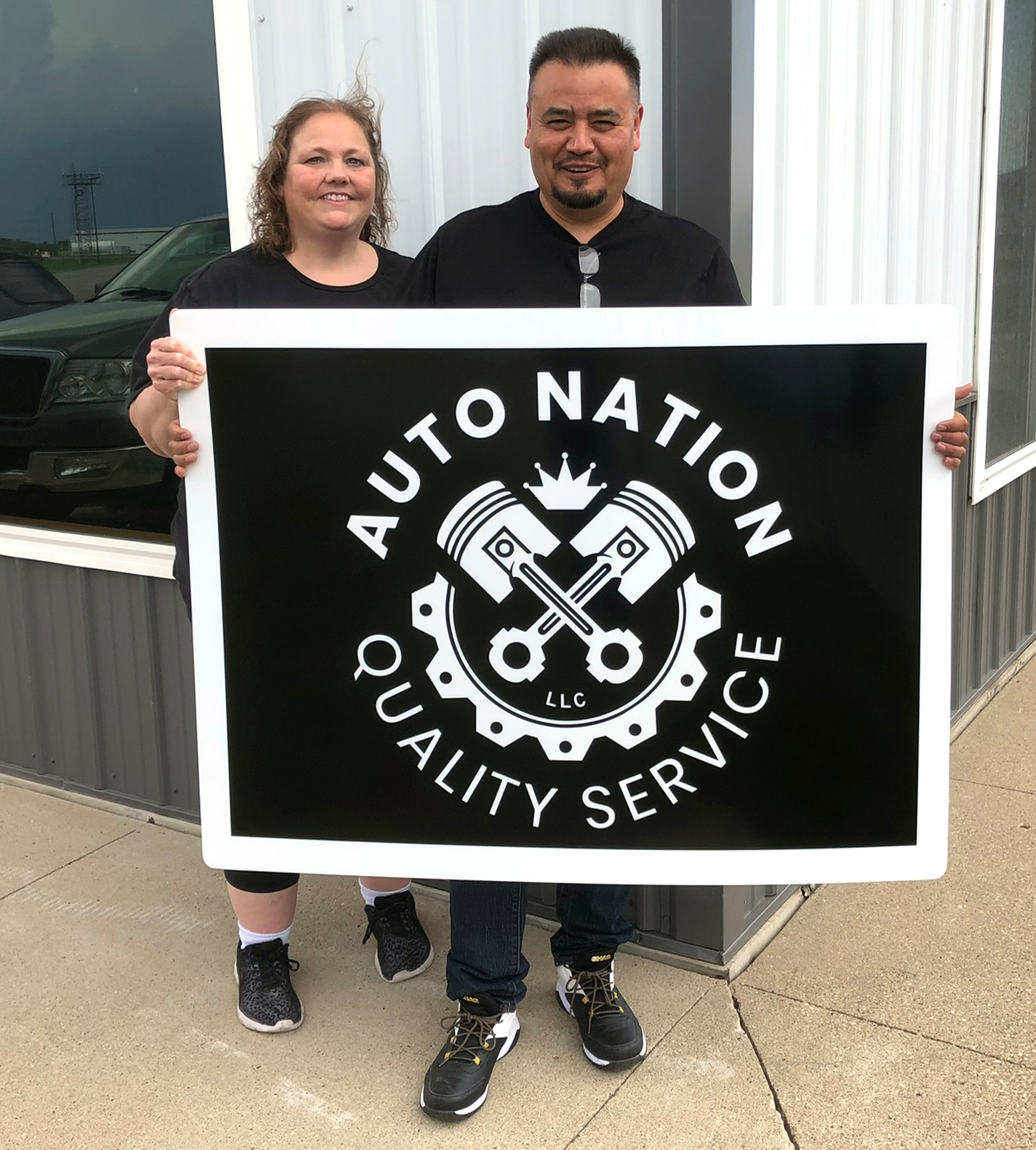 Businesses owners hold up sign saying "Auto Nation Quality Service" 