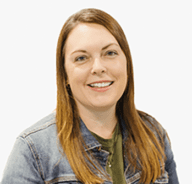 A woman with straight, light brown hair wearing a denim jacket over a green top, smiling at the camera against a plain white background.