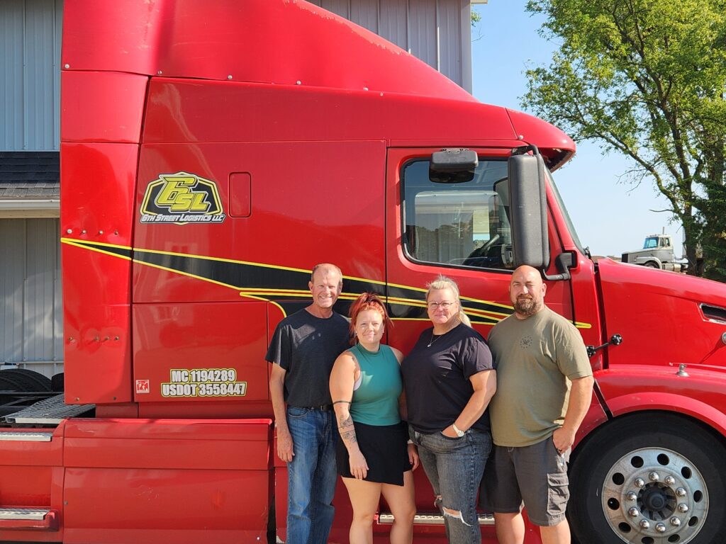 Pictured are 6th Street Logistics’ office team in front of a bright red semi truck.