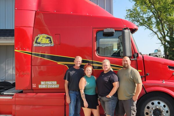 Pictured are 6th Street Logistics’ office team in front of a bright red semi truck.