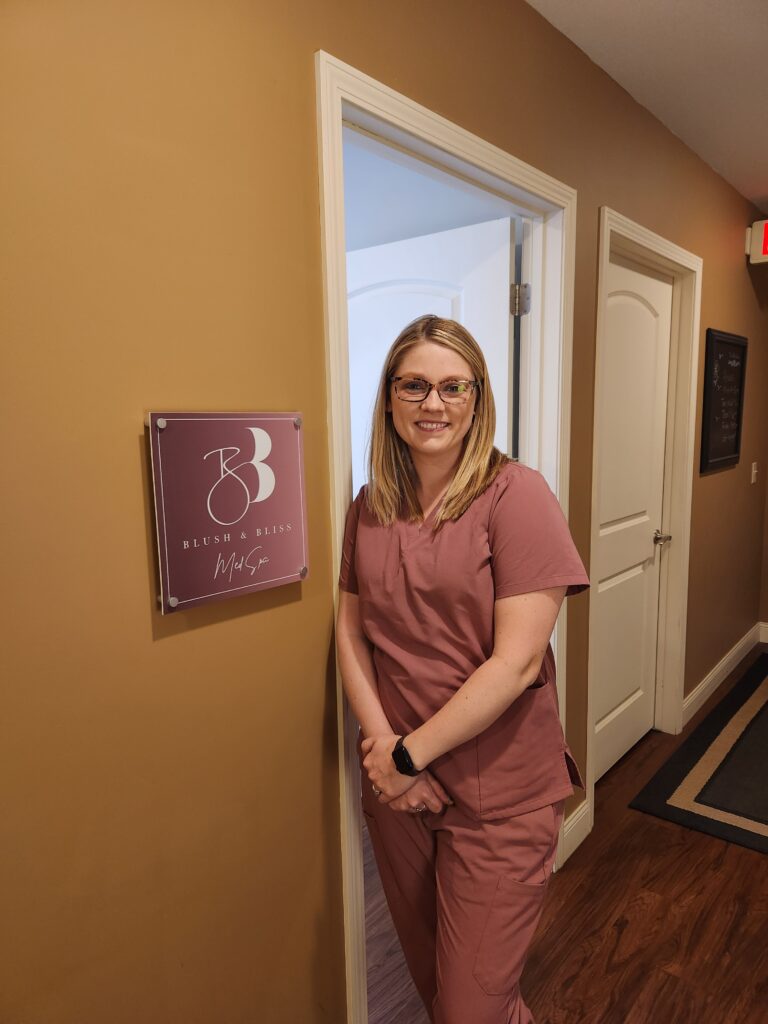 Maisie Hagert stands in the doorway at Blush & Bliss Med Spa wearing mauve scrubs.