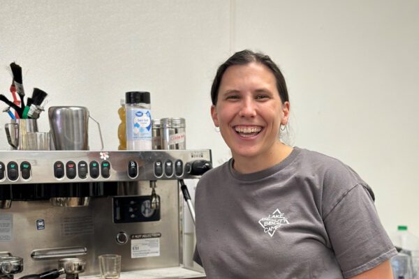 Emma stands inside her shop next to a commercial espresso machine.