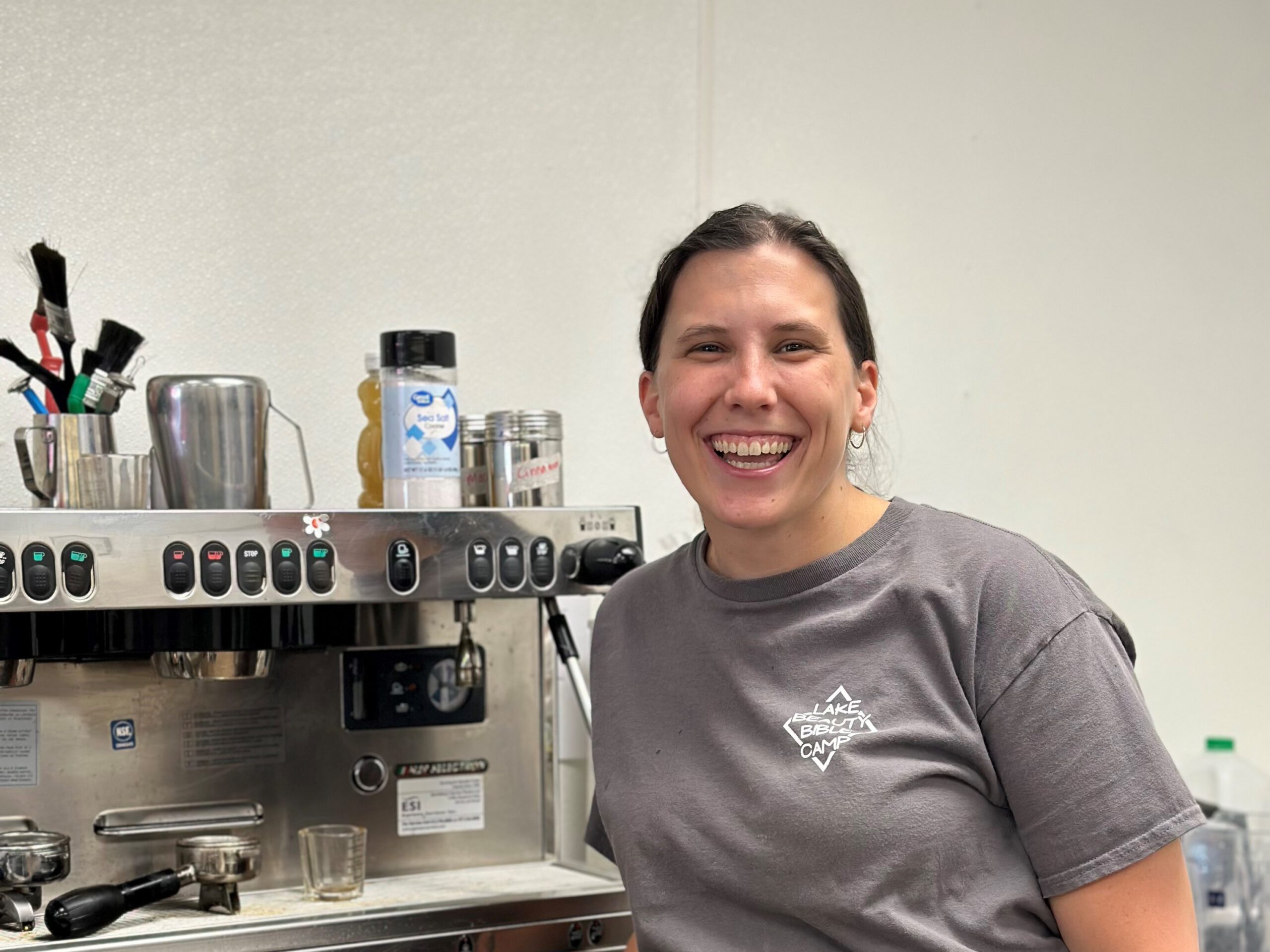 Emma stands inside her shop next to a commercial espresso machine.