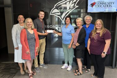 Seven adults stand indoors in front of a sign reading Jefferson Learning Center. In recognition of Patricia Dols board service, one man receives a check from a woman; everyone is smiling. A screen in the background displays Willmar Community Education.