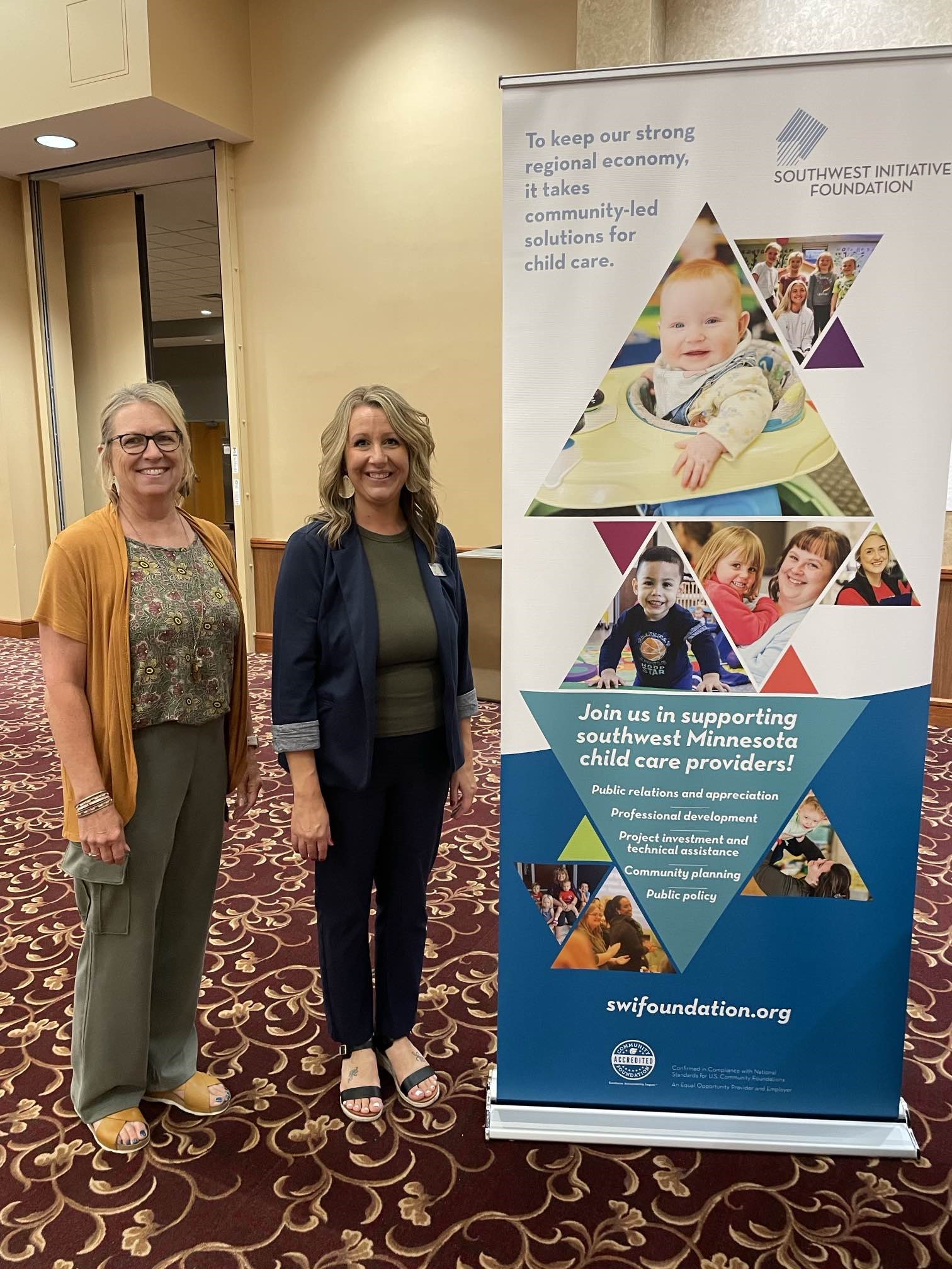 Cheryl and Briana next to a pop-up banner at the child care listening session in Granite Falls.