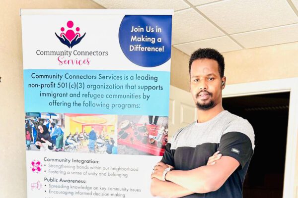 Abdifatah Mohamed stands next to a banner for the Willmar nonprofit Community Connector Services.