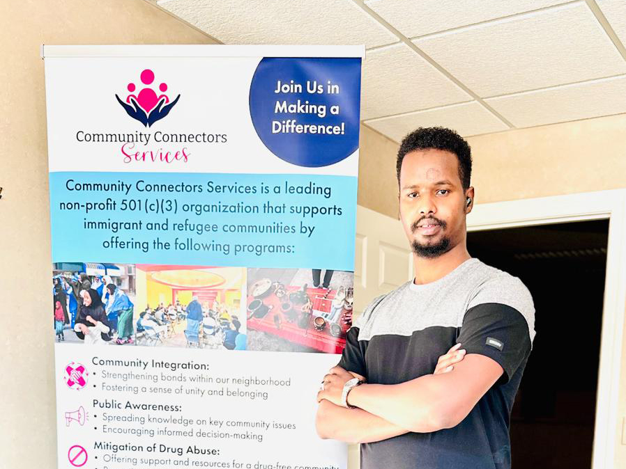 Abdifatah Mohamed stands next to a banner for the Willmar nonprofit Community Connector Services.