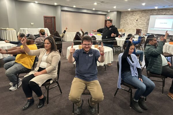 Emerging leaders sit facing outward in a circle of chairs, holding a network of strings tied together.