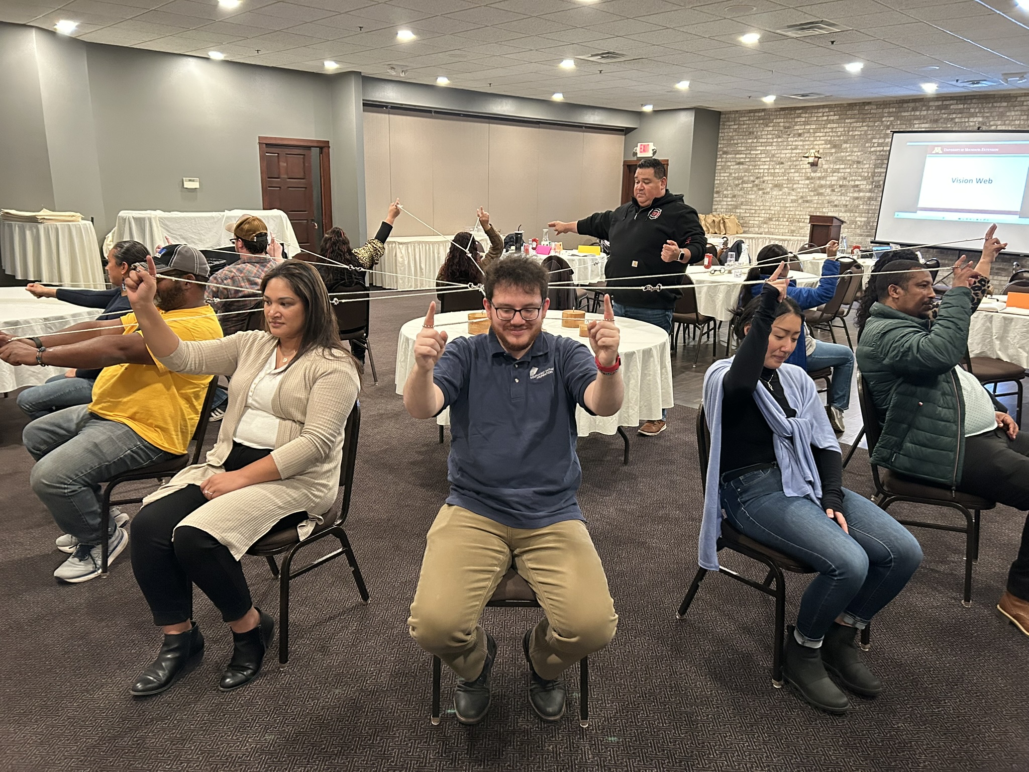 Emerging leaders sit facing outward in a circle of chairs, holding a network of strings tied together.