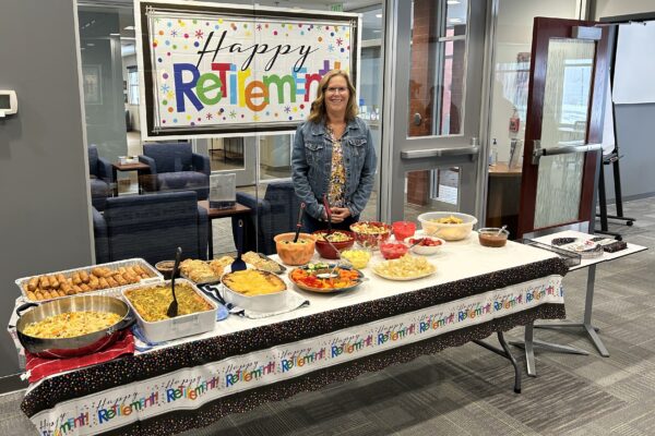 Jackie Turner stands in front of a Happy Retirement banner behind a table of potluck dishes.