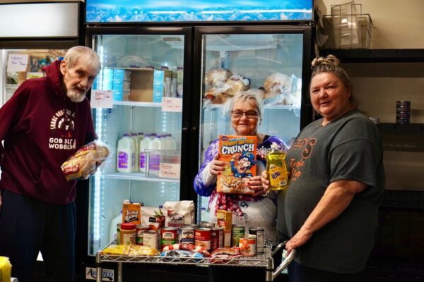 A group of three people display donations to the Loaves & Fishes food shelf.