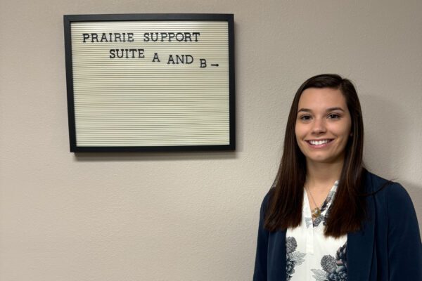 Jessica Schoborg stands next to an indoor sign for Prairie Support Services.