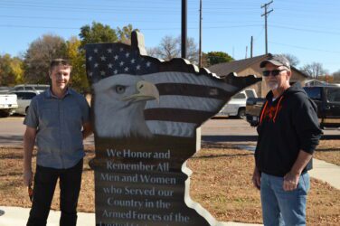 Tony and Marv stand on either side of a monument carved in the shape of Minnesota.