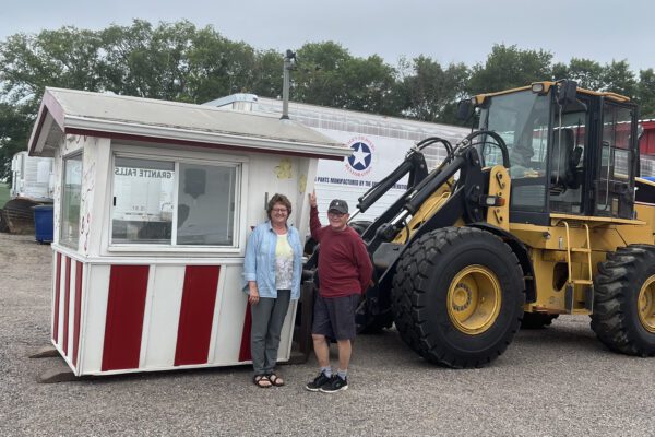 Judy and Tom in front of the popcorn box-shaped stand loaded onto the forks of a tractor attachment